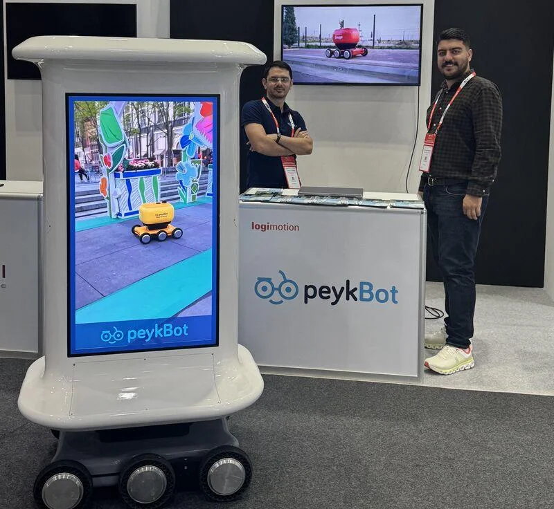 Mobile robot with a tall display screen beside two exhibitors at an exhibition stand