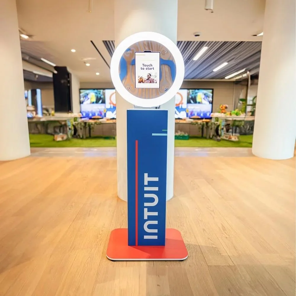 Photo booth kiosk with a ring light and touch-to-start screen on a wooden floor