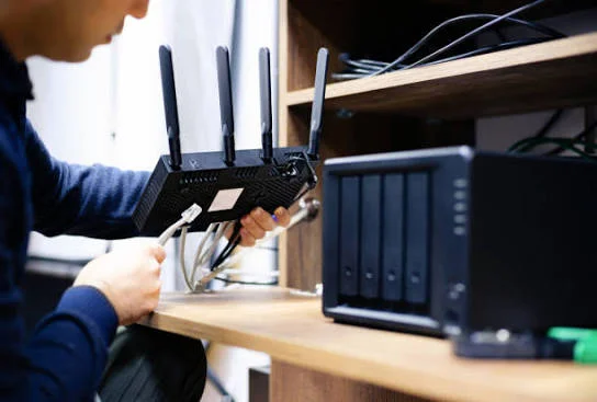 Installing WiFi in Dubai 26 Engineer connecting an ethernet cable to a WiFi router and network storage device in Dubai